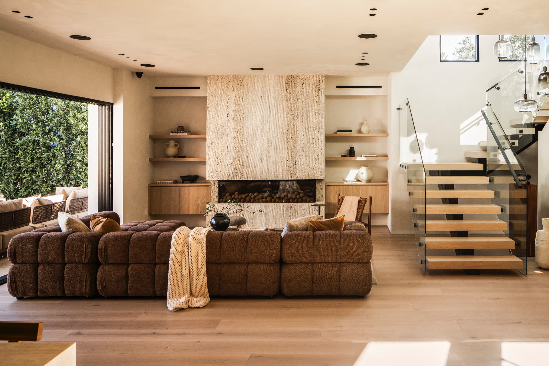 Living room with a stone fireplace surround beside a floating oak staircase with a glass railing