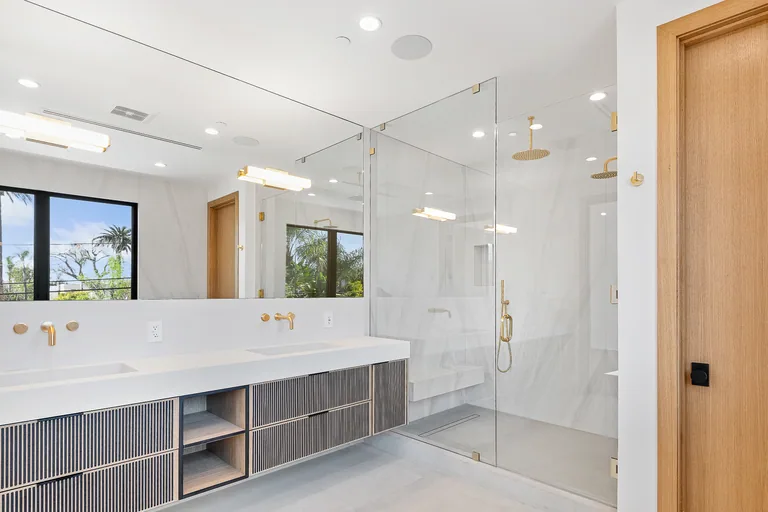 Primary bathroom with a marble double vanity, fluted cabinet fronts, brass fixtures and a glass-enclosed walk-in shower