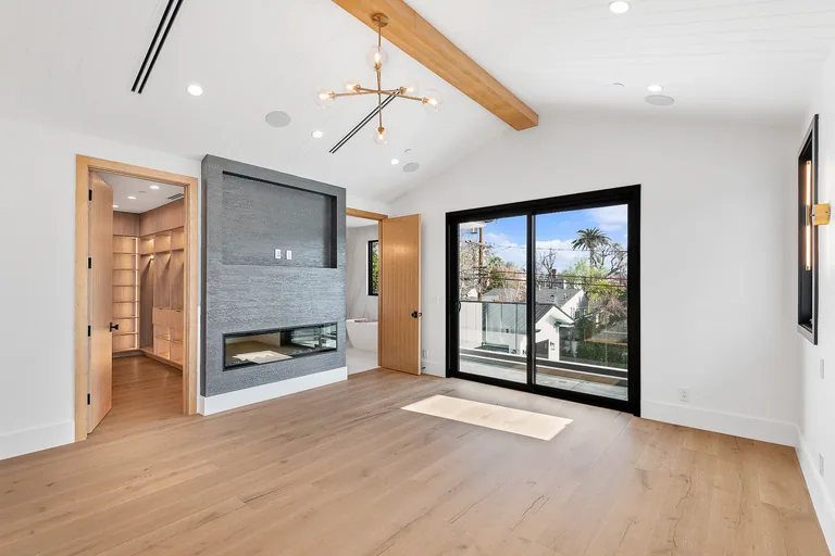 Primary bedroom with a vaulted ceiling, exposed wood beam, linear fireplace and sliding glass doors onto a balcony