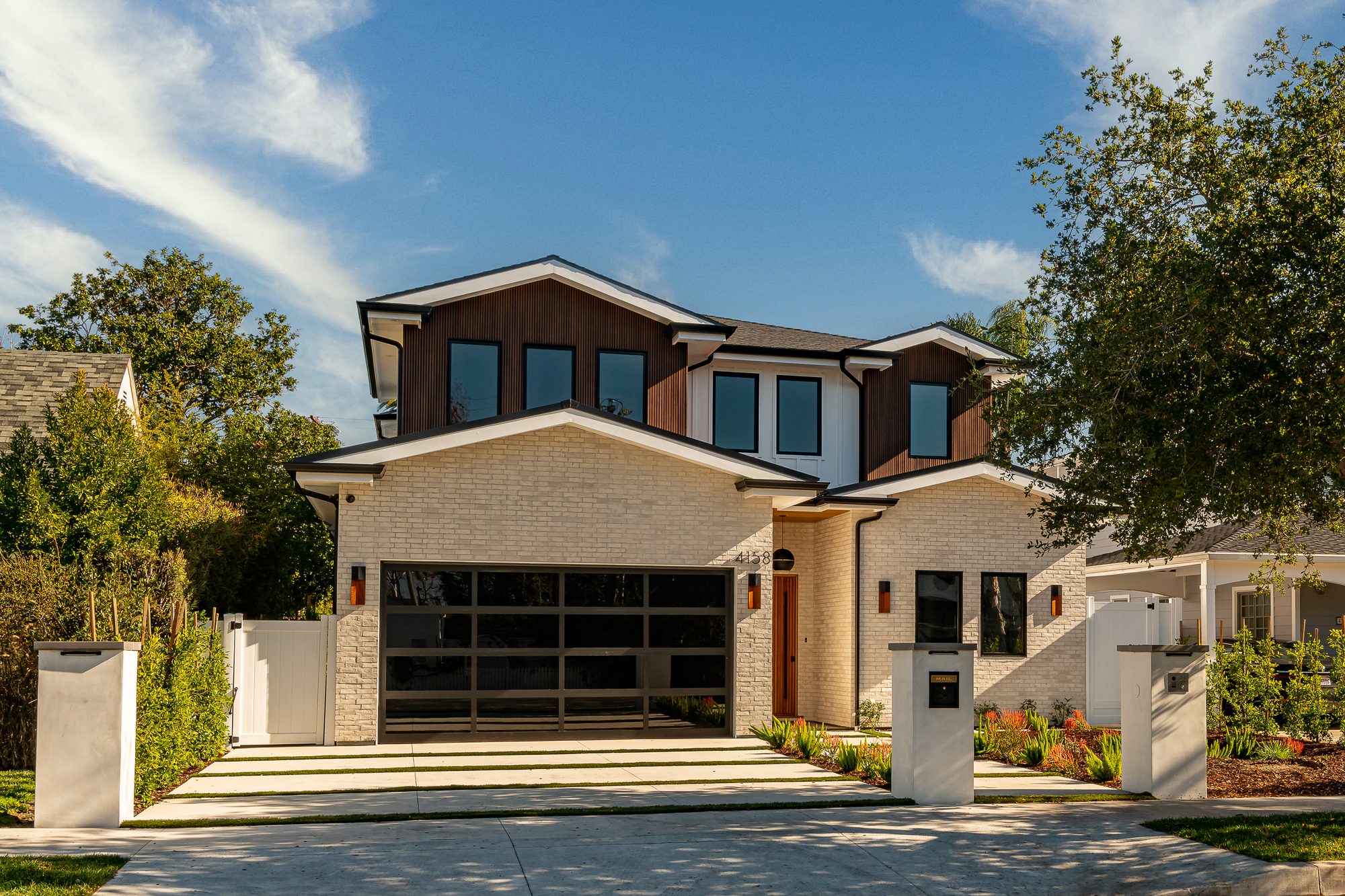 Front elevation of a two-story custom home in Studio City with white brick, dark wood-clad gables and a glass garage door