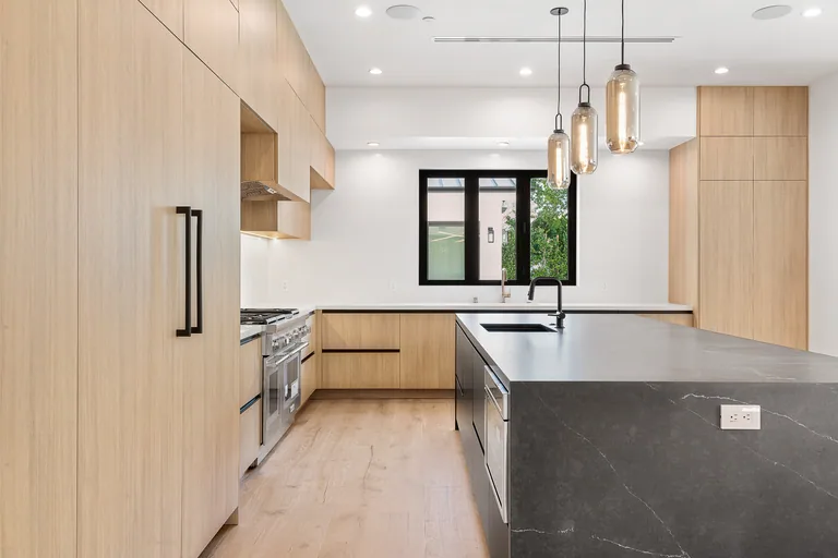 Contemporary kitchen in Studio City with white oak cabinetry, integrated appliances and a black stone waterfall island