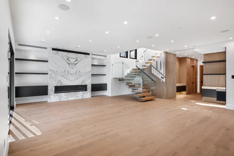 Open living room with a full-height marble fireplace surround, built-in shelving and a floating oak staircase with glass railing