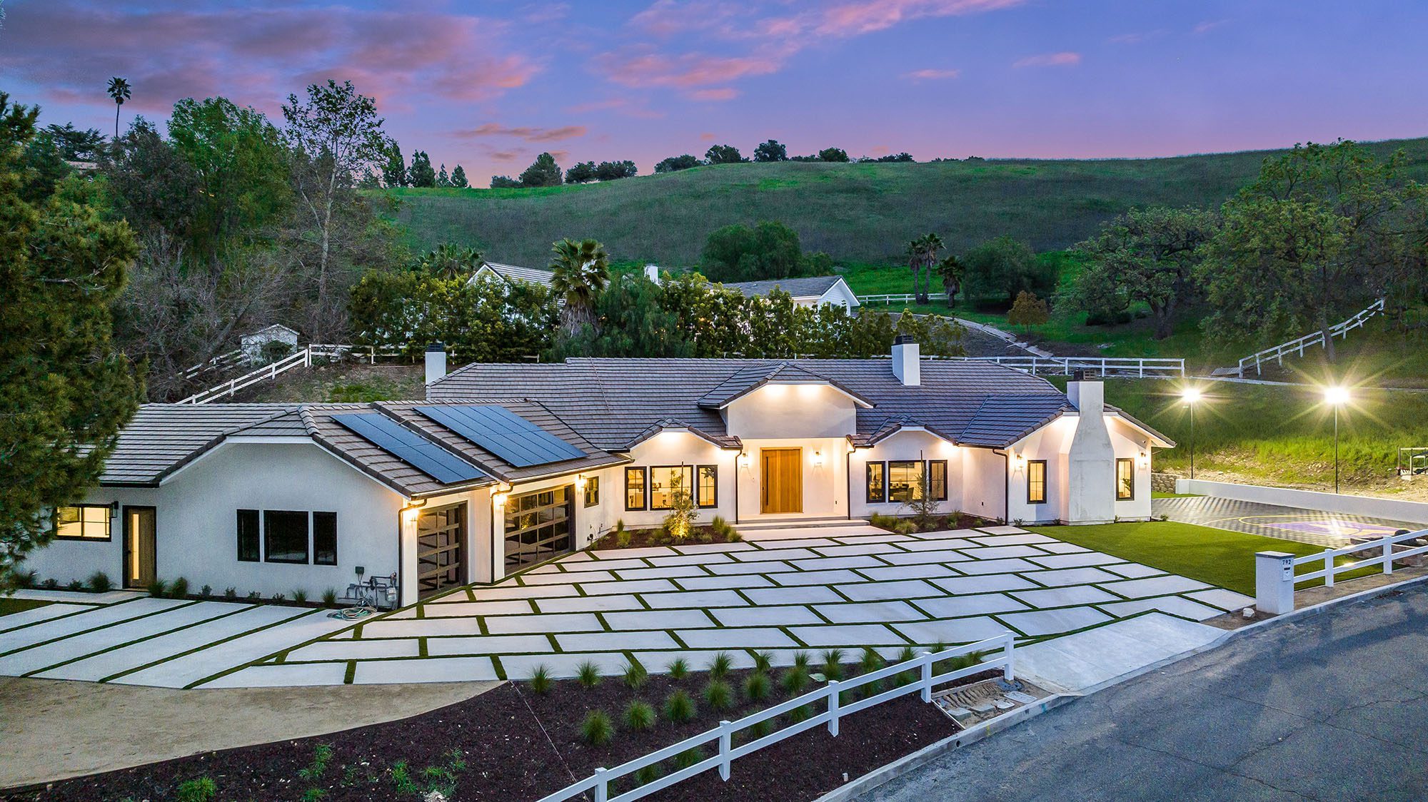 Aerial dusk view of a single-story tile-roof home in Thousand Oaks with a paver driveway, solar panels and hillside setting