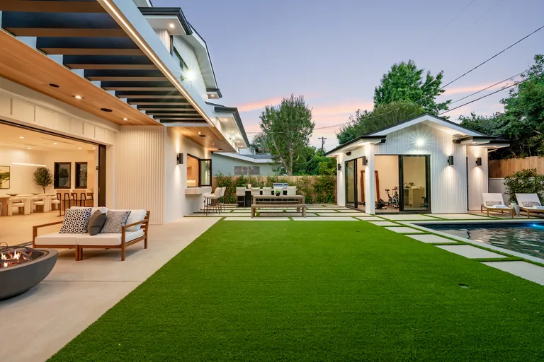 Backyard at dusk with a lawn, covered outdoor lounge, built-in barbecue, pool and detached guest cabana