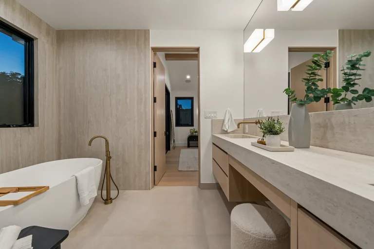 Bathroom clad in travertine with a freestanding soaking tub, brass floor-mounted filler and a floating double vanity