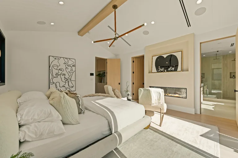 Primary bedroom with a vaulted ceiling, wood beam, plaster fireplace surround and an ensuite bathroom beyond