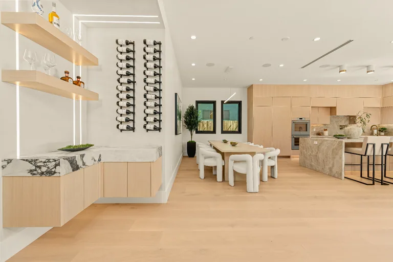 Dining area with a built-in wet bar, backlit floating oak shelves and a wall-mounted wine rack beside the open kitchen