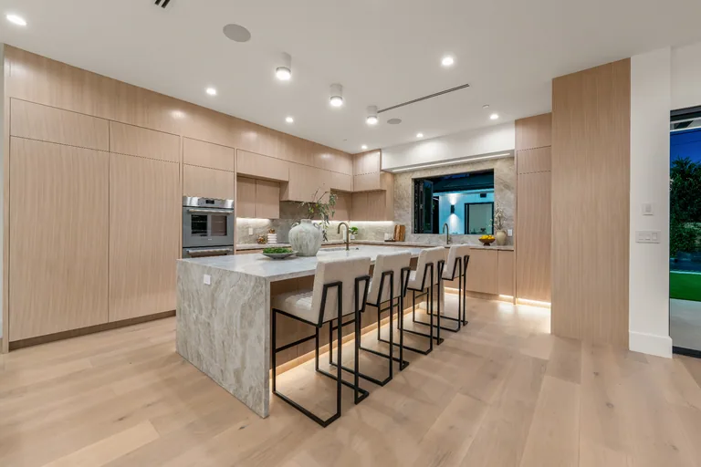 Kitchen with full-height white oak cabinetry, integrated appliances and a stone waterfall island seating four
