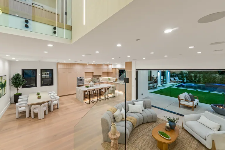 Double-height great room in Studio City combining the open kitchen, dining area and living room, with glass walls onto the pool