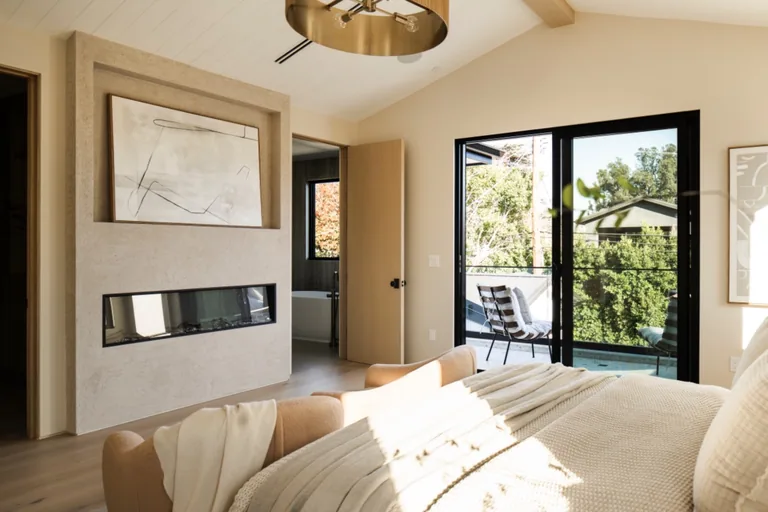 Primary bedroom with a plaster fireplace surround, vaulted ceiling and black-framed sliding doors onto a deck