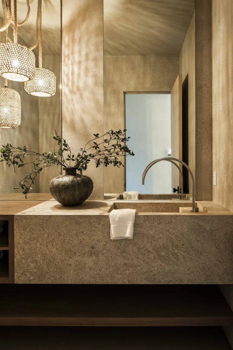 Powder room with limewashed plaster walls, a carved stone trough sink and beaded glass pendants