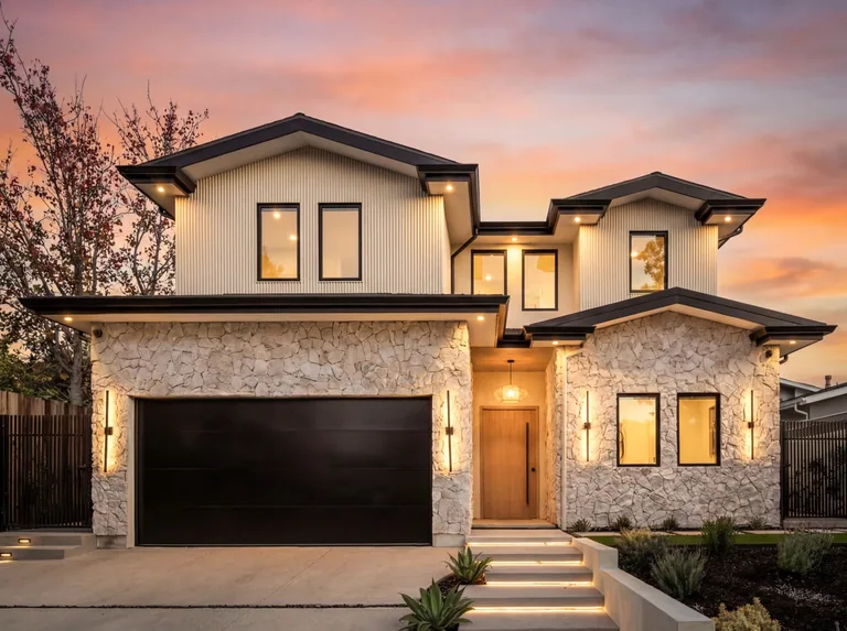 Front elevation of the new home at 4140 Kraft Ave in Colfax Meadows at sunset, with a stacked stone base, board-and-batten siding and a black garage door