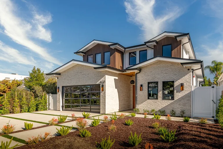Front elevation of the newly built home at 4158 Beck Ave in Studio City, with white brick, wood-clad gables, a glass garage door and drought-tolerant landscaping