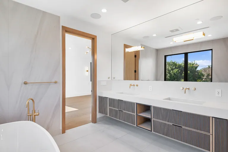 Primary bathroom with a fluted double vanity, brass wall-mounted faucets and a freestanding tub