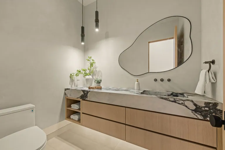 Powder room with a veined marble waterfall vanity, oak drawers and an organic-shaped mirror