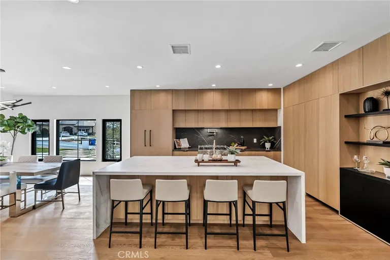 Open kitchen with white oak cabinets, a dark tile backsplash and a stone island seating four