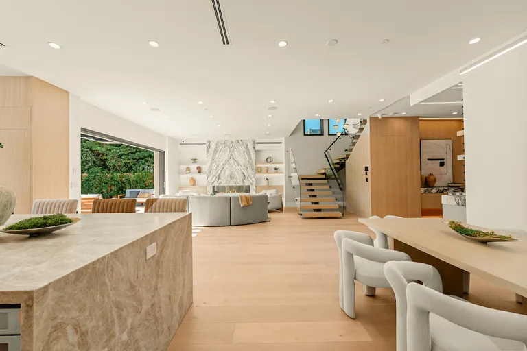 Open living and dining area with a stone fireplace wall, oak staircase and floor-to-ceiling glass